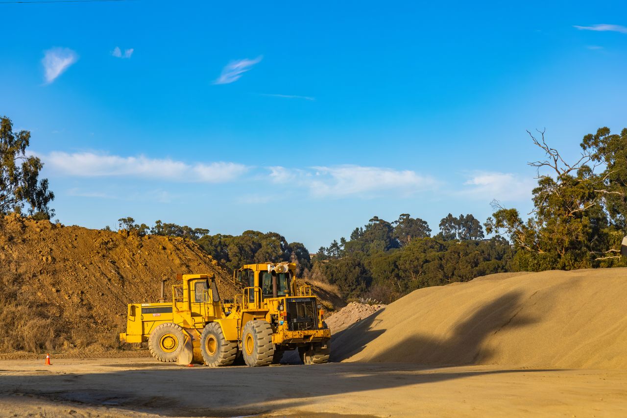 Services A large yellow tractor at a construction site with gravel and sand piles under a clear blue sky.