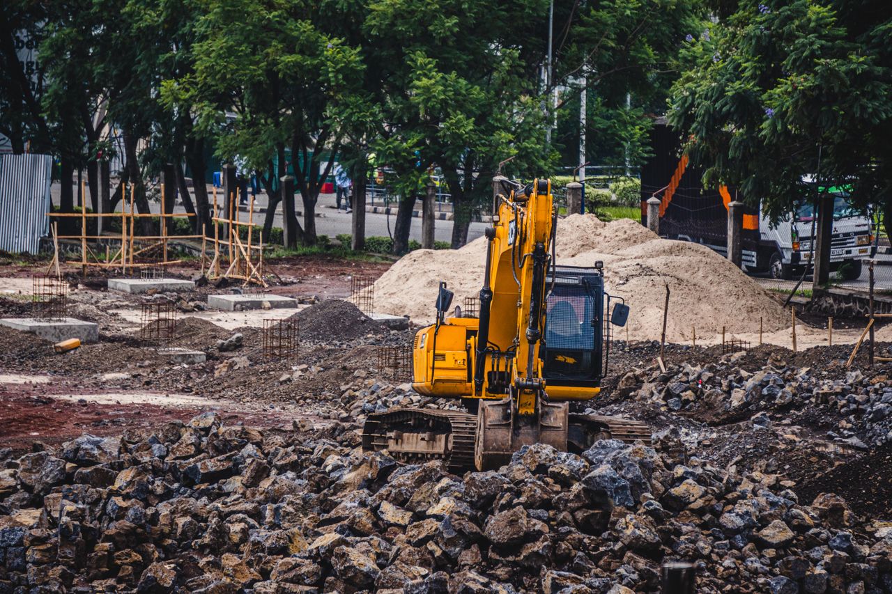 Services A yellow excavator working at an urban construction site surrounded by rocks and trees.