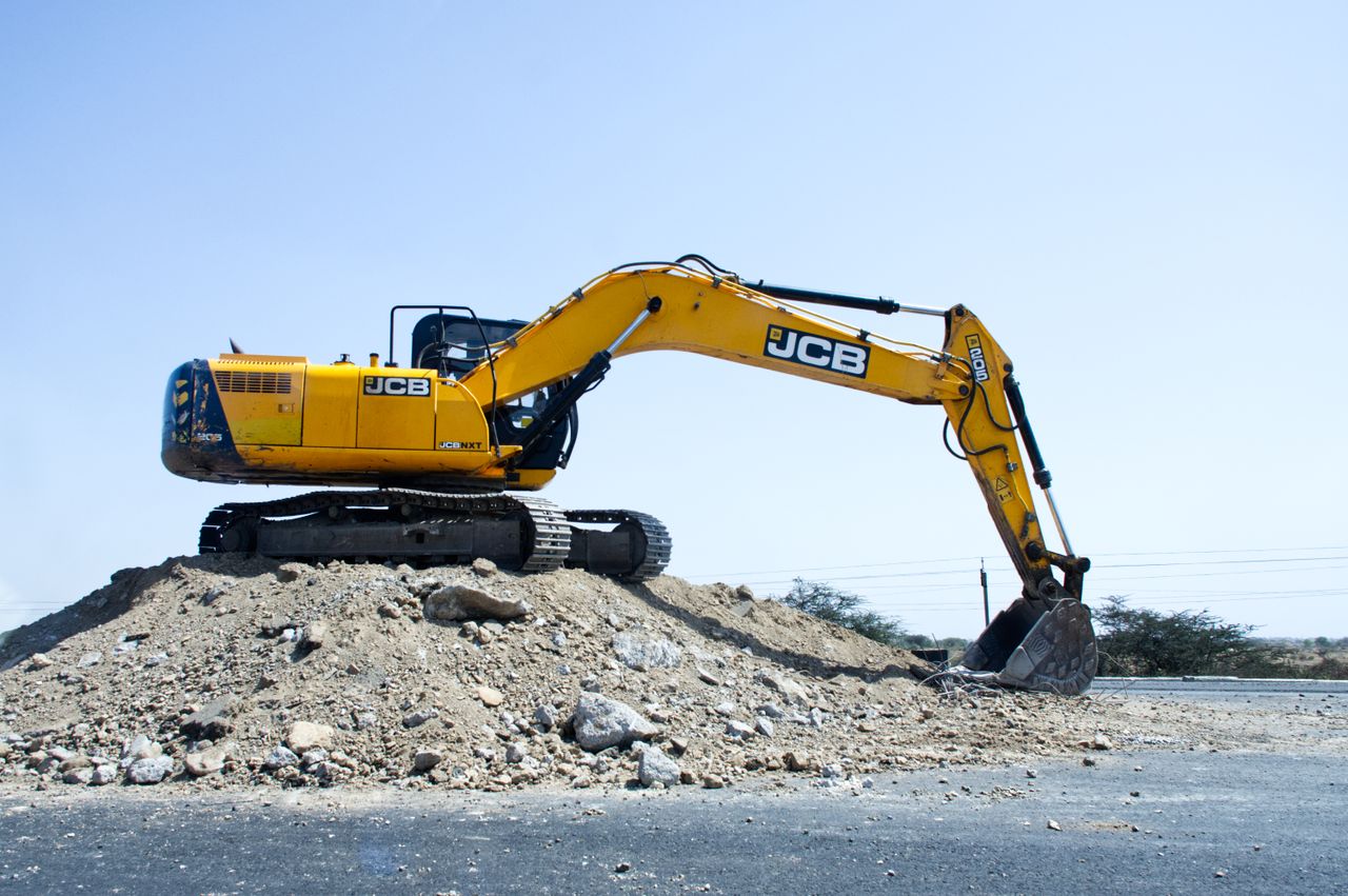 About Yellow excavator on a pile of dirt at a construction site under clear blue sky.