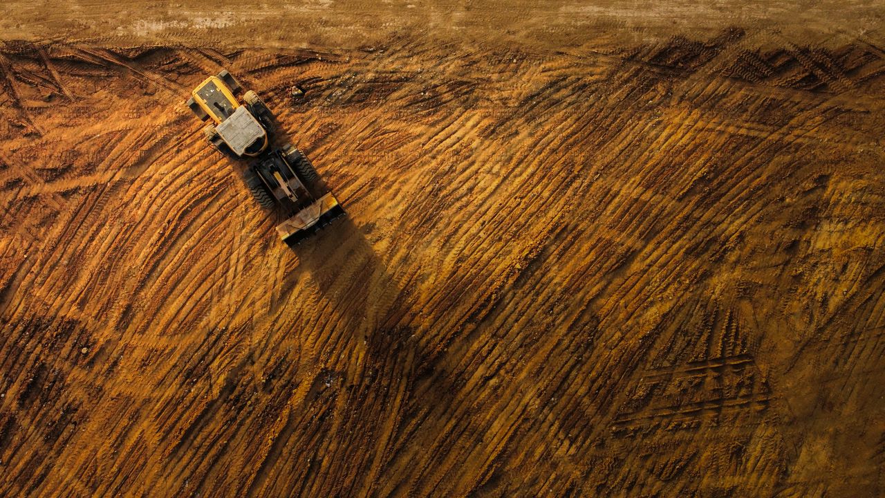 Services Top-down view of a bulldozer moving earth on a large construction site.