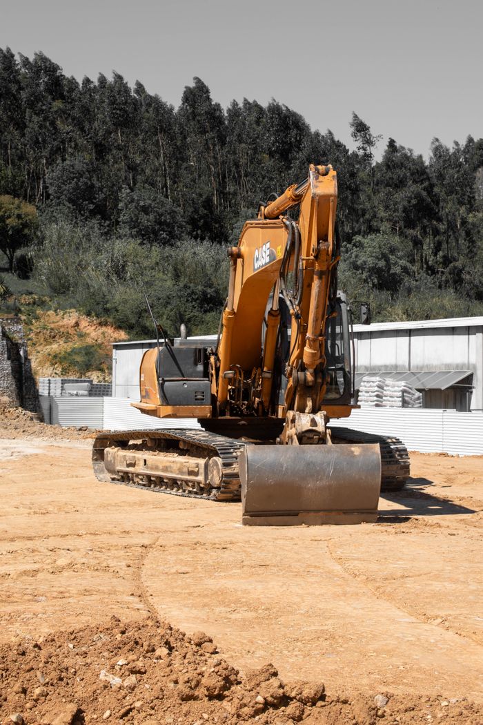 Services Large orange excavator on a construction site with trees in the background.